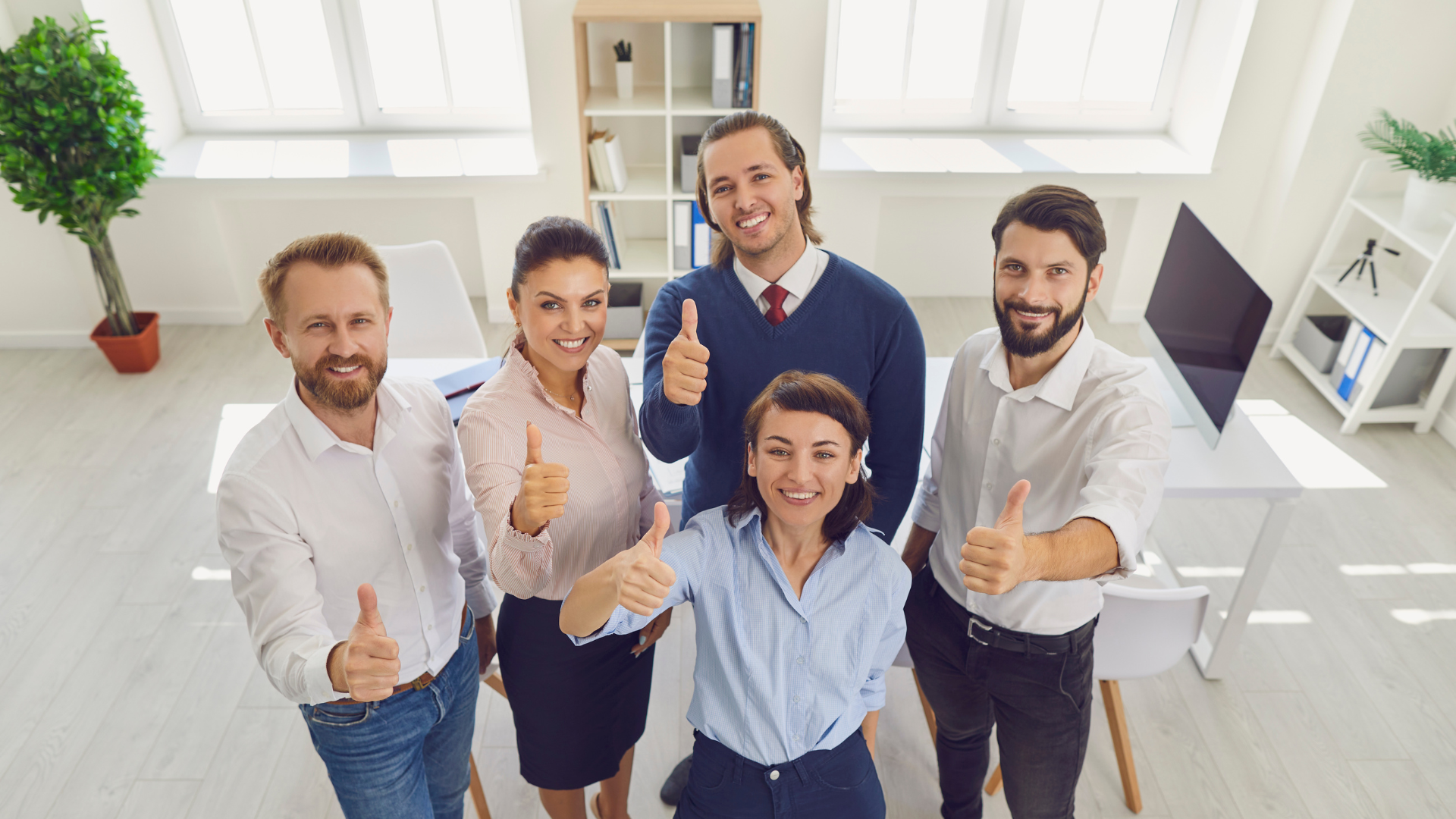 Fünf Büroangestellte lächeln in die Kamera mit Daumen hoch