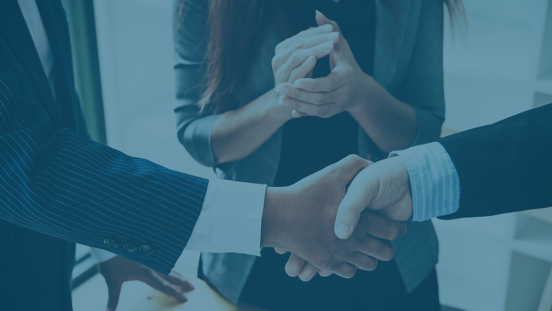 Handschlag zweier Personen im Business Dress, eine dritte Person beklatscht ihn
